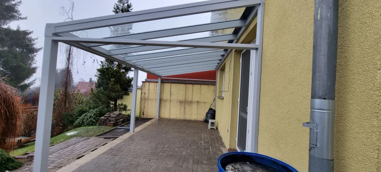 Pergola moderne LIGHT en aluminium gris avec toit en verre, fixée au mur de la maison au-dessus de la terrasse