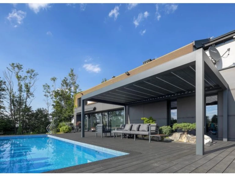 Pergola bioclimatique moderne SUNBEAM 1400 de couleur grise, installée sur la terrasse près de la piscine et équipée d'un coin salon extérieur