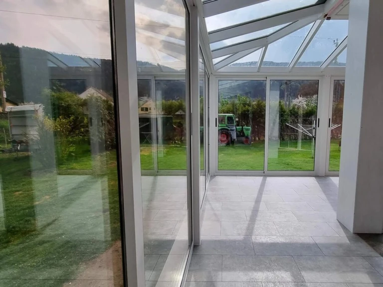Vue depuis l'intérieur sur la terrasse vitrée avec le jardin et le tracteur en arrière-plan