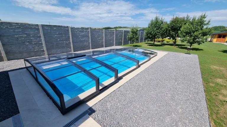 Un abri de piscine moderne et bas, avec une structure anthracite, dans le jardin