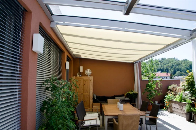 Une terrasse moderne avec un coin repas sous un auvent en tissu rétractable et une verrière.