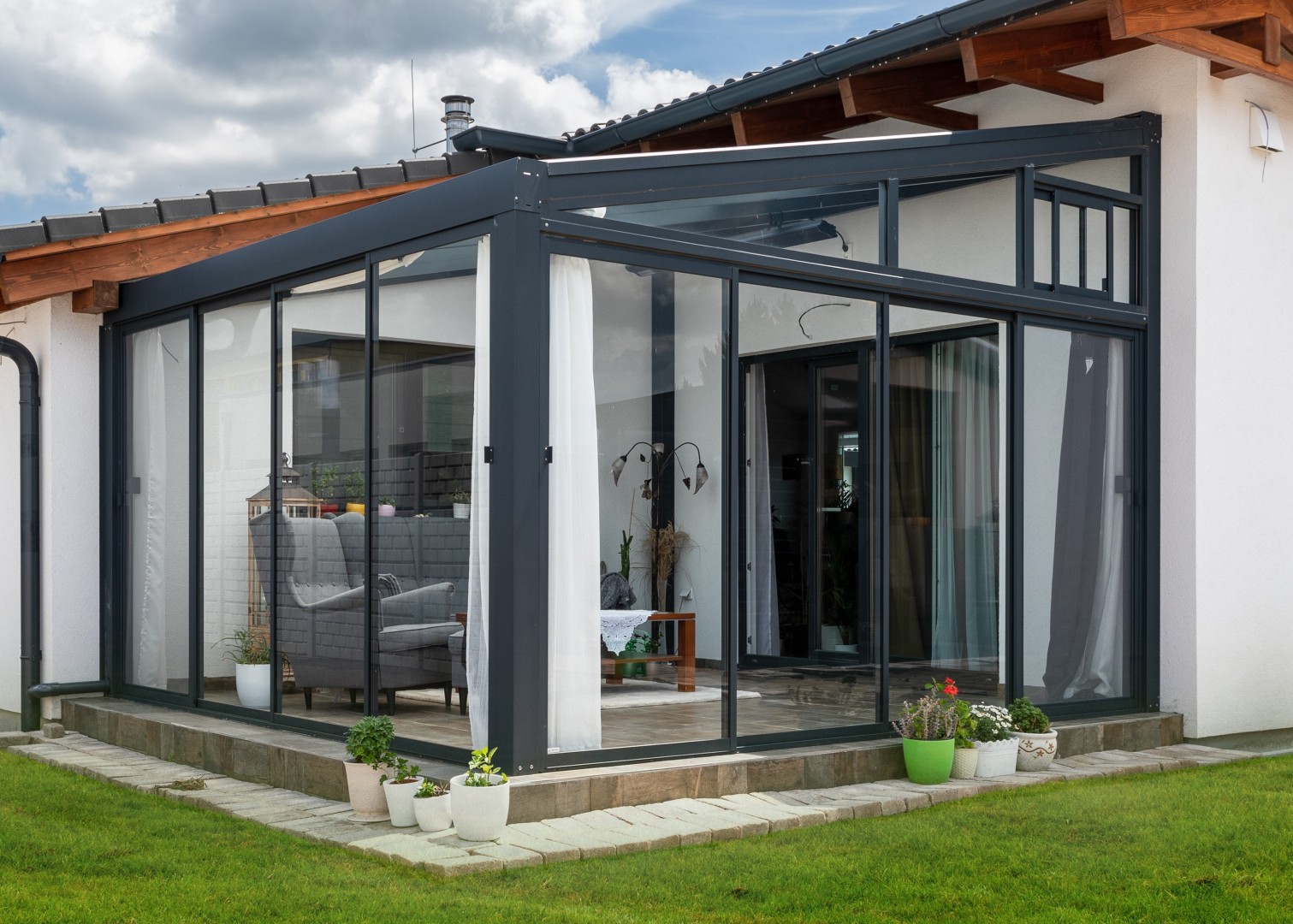 Une pergola moderne en aluminium et verre, attenante à la maison, avec un mobilier d'intérieur élégant.