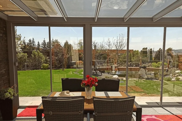 Une terrasse vitrée donnant sur le jardin, avec un coin salon et des fleurs