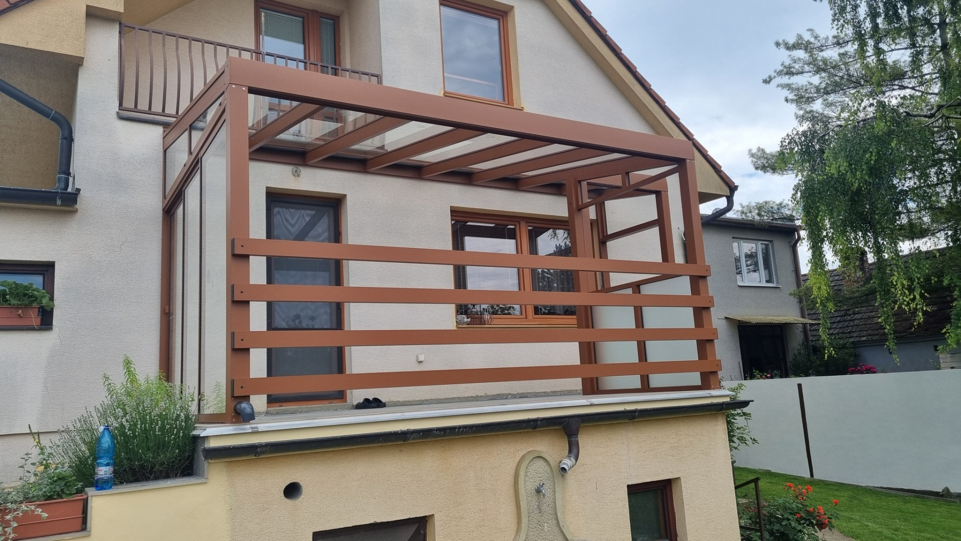 Pergola atypique en aluminium marron avec toit en verre et brise-soleil latéral sur le balcon d'une maison individuelle