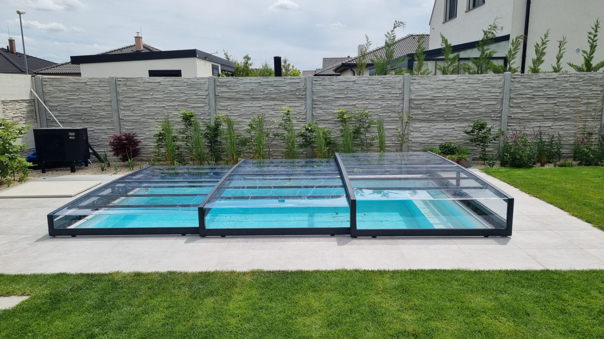 Un abri de piscine moderne et bas, doté d'une structure anthracite et d'un matériau de remplissage transparent, installé dans le jardin d'une maison individuelle.