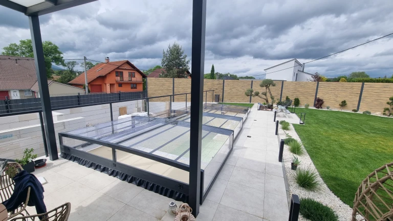 Vue sur la toiture basse et moderne d'une piscine dans un jardin aménagé, sous un ciel nuageux.