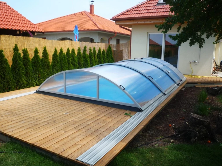 Abri de piscine bas et fermé sur une terrasse en bois près d'une maison individuelle