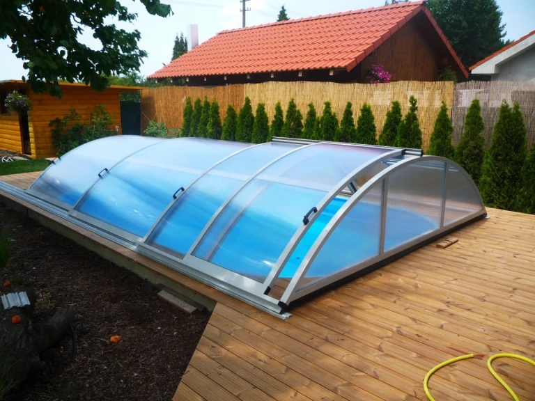 Petite verrière en arc au-dessus de la piscine, sur une terrasse en bois dans le jardin