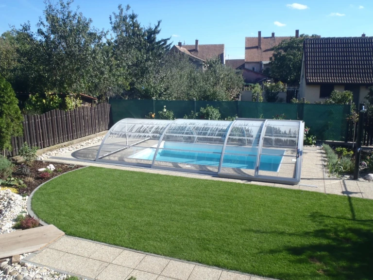 Une couverture moderne et basse pour la piscine située dans le jardin d'une maison individuelle avec pelouse.
