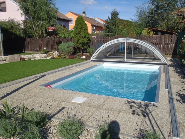 Une piscine moderne dans le jardin, dotée d’un auvent en arc en retrait et d’un espace aménagé autour.