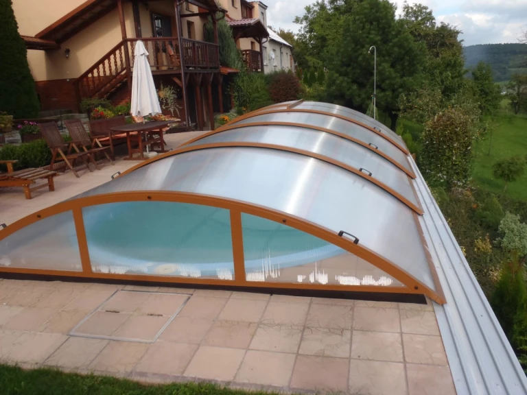 Abri de piscine fermé de type KLASIK, à structure arquée de couleur marron, installé dans le jardin d'une maison individuelle.