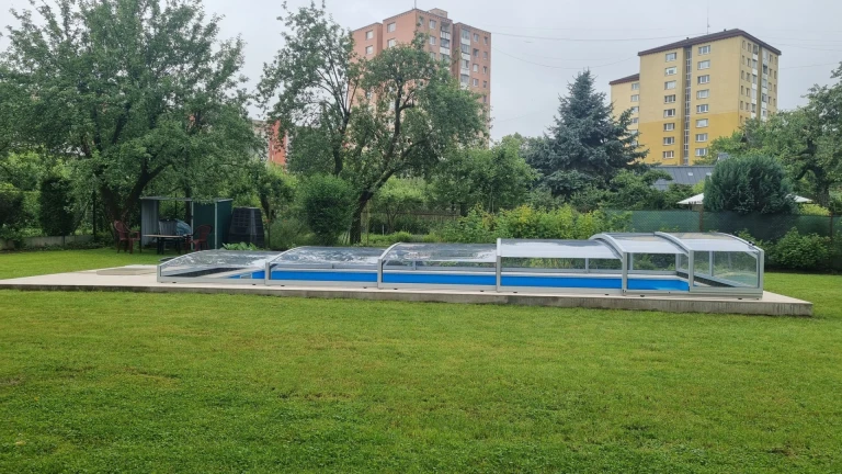 Une couverture de piscine basse PREMIER dans un jardin à Martin, avec une pelouse verte et des immeubles d'habitation en arrière-plan