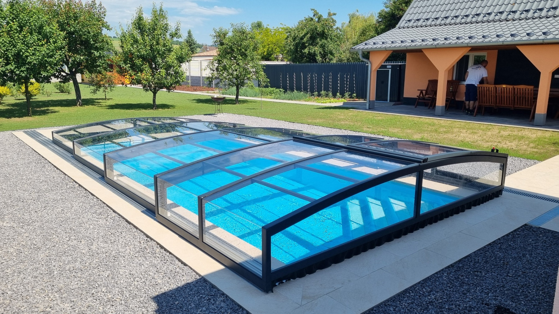 Une couverture de piscine moderne et basse de la gamme PREMIER, dotée d'un cadre foncé, dans le jardin d'une maison individuelle.