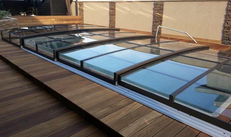 Une couverture de piscine basse de couleur anthracite, avec des panneaux transparents, installée sur une terrasse en bois
