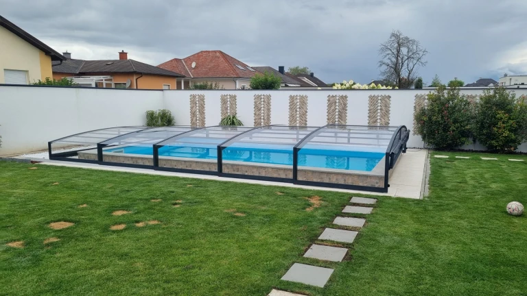 Une couverture de piscine moderne et basse de type STAR, avec une structure noire, dans le jardin d'une maison individuelle.