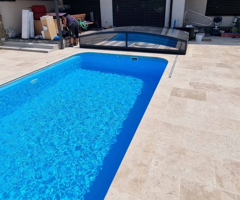 Une piscine moderne aux eaux bleues cristallines, dotée d'une couverture noire partiellement ouverte, située sur une terrasse pavée.