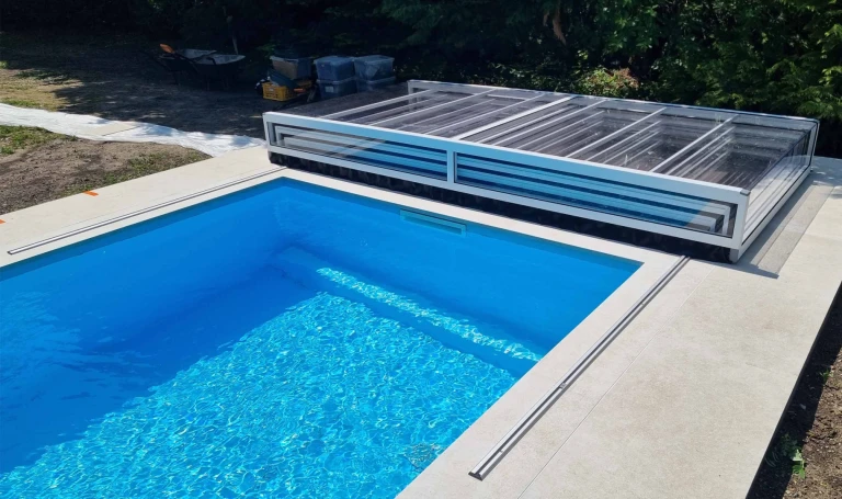Une piscine bleue moderne équipée d'un abri blanc sans rails EXCLUSIVE, replié sur le rebord de la piscine.