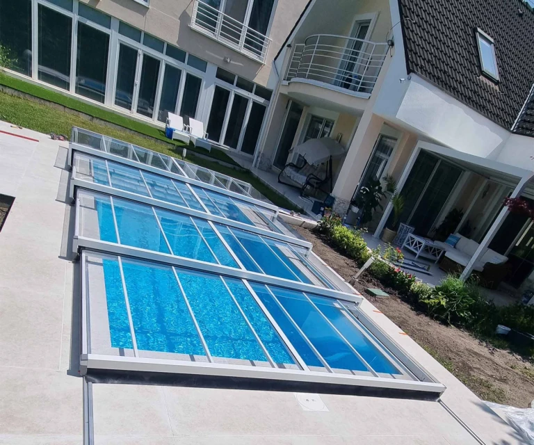 Une couverture de piscine moderne sans rails, modèle EXCLUSIVE, avec un revêtement transparent, devant une maison individuelle.