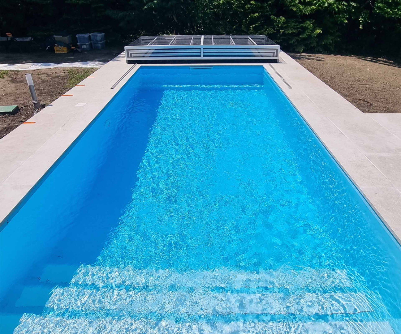 Une piscine rectangulaire moderne, aux eaux d'un bleu éclatant et dotée d'une élégante bordure blanche, dans le jardin.
