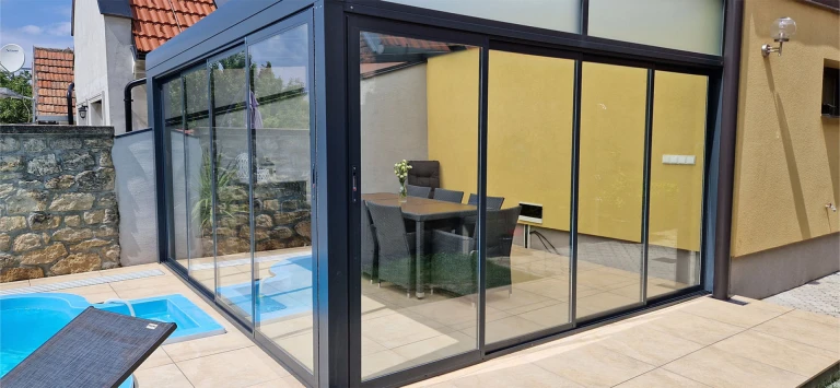 Une véranda moderne vitrée, dotée d'une structure anthracite, construite à côté de la piscine, près de la maison.