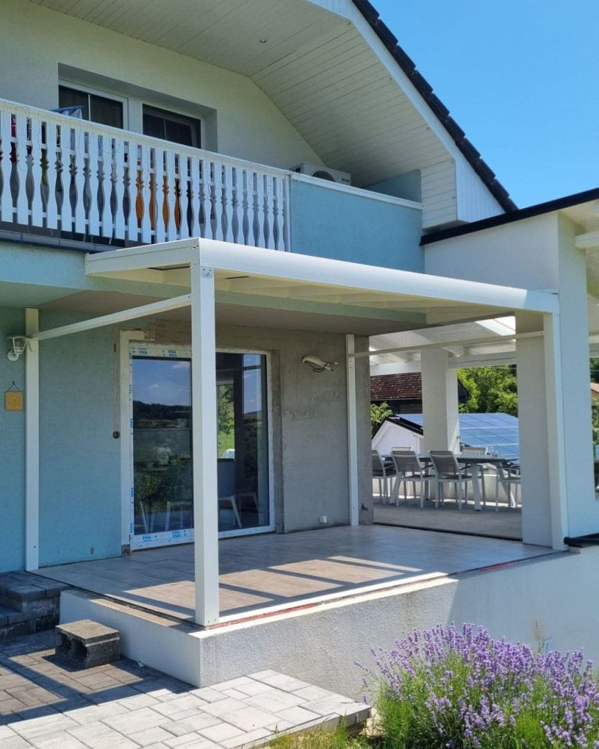 Une pergola moderne en aluminium blanc attenante à une maison individuelle, avec une terrasse et de la lavande au premier plan