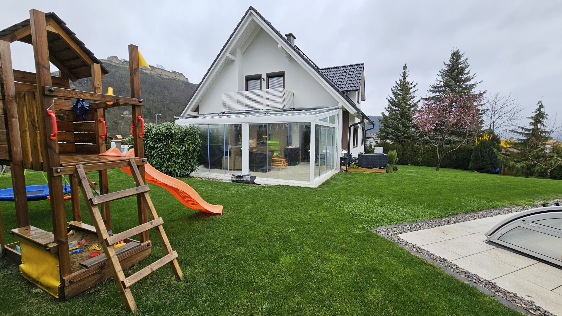 Maison familiale moderne avec pelouse, aire de jeux pour enfants et annexe vitrée.