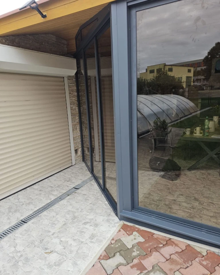 Détail du raccord d'angle d'une baie vitrée moderne de terrasse, dans un cadre anthracite, à côté de la porte de garage.