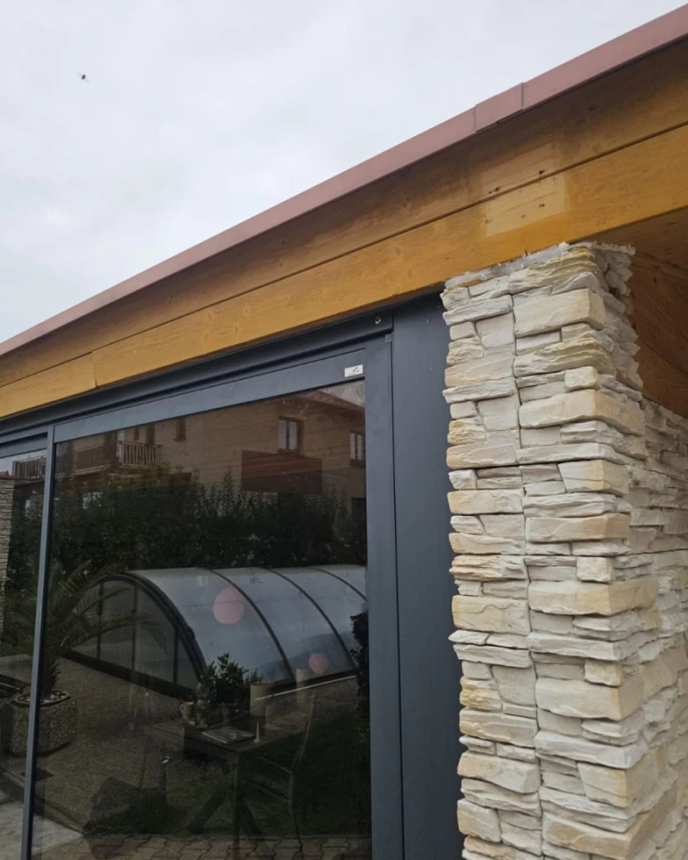 Détail du raccordement de la baie vitrée de la terrasse au revêtement en pierre et à la charpente en bois.