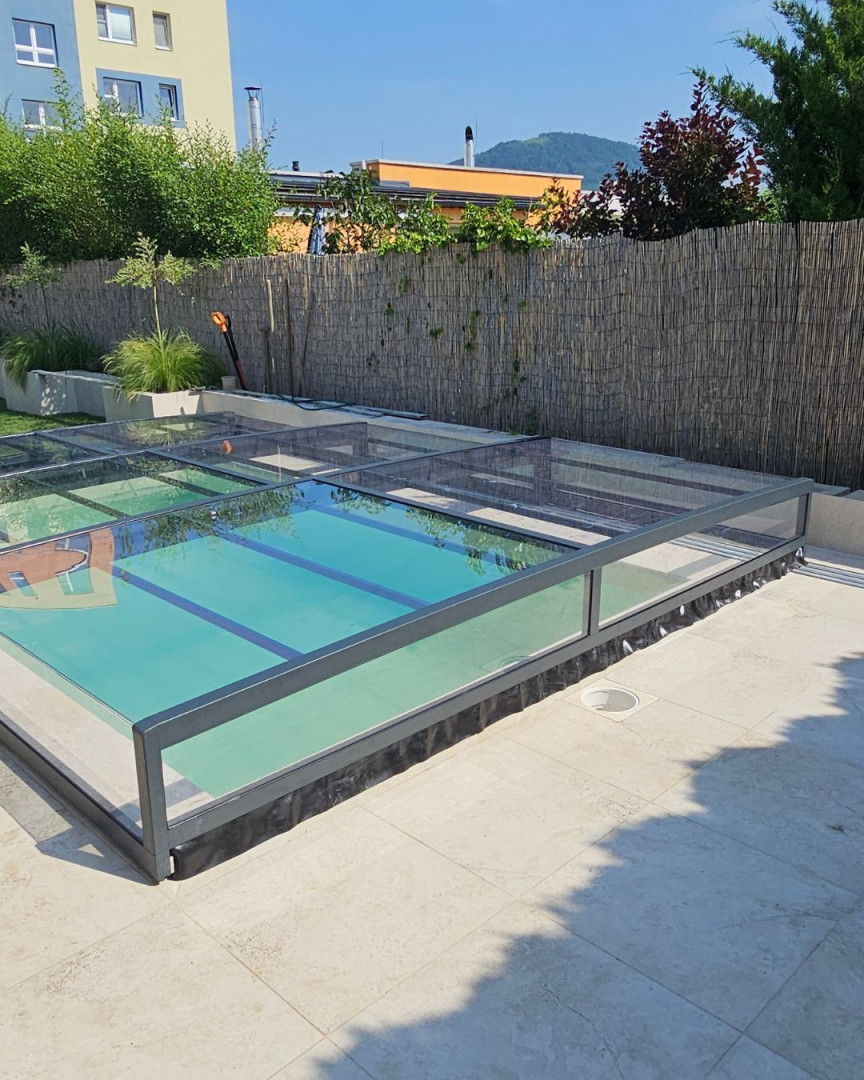Une couverture de piscine moderne, basse et vitrée, avec un cadre anthracite, installée sur une terrasse pavée.