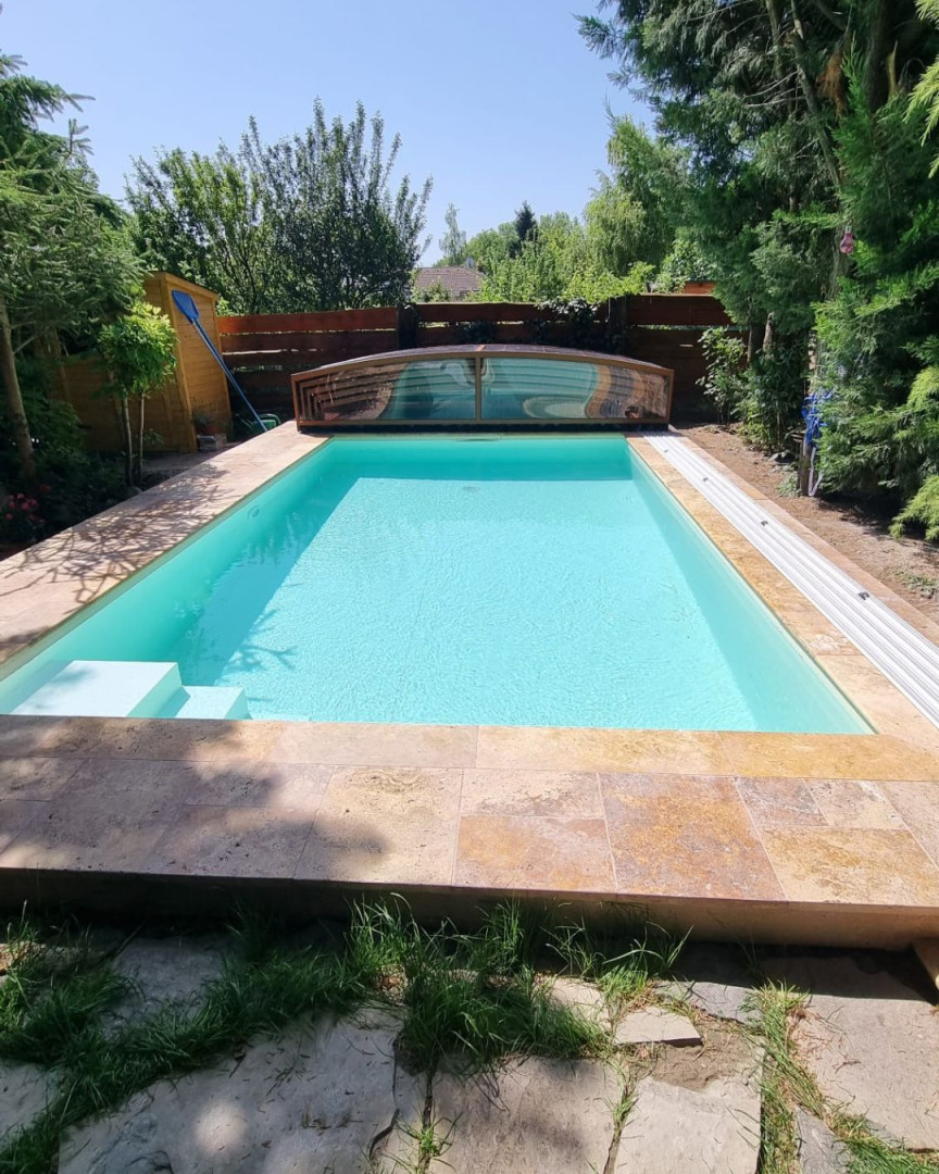 Une piscine moderne aux eaux turquoise cristallines, surmontée d'un abri coulissant bas, dans le jardin.