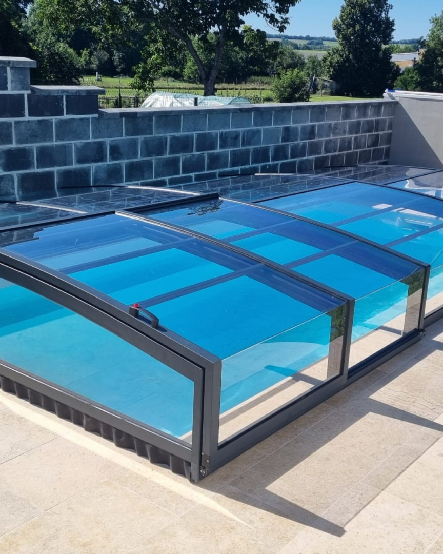 Une couverture de piscine moderne et basse, dotée de panneaux transparents, dans le jardin