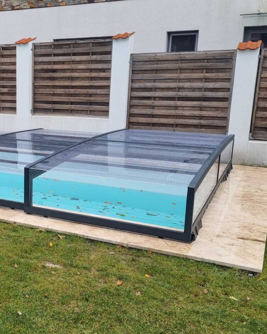 Une couverture de piscine moderne et basse, dotée d'un cadre anthracite et de polycarbonate transparent, dans le jardin d'une maison individuelle.