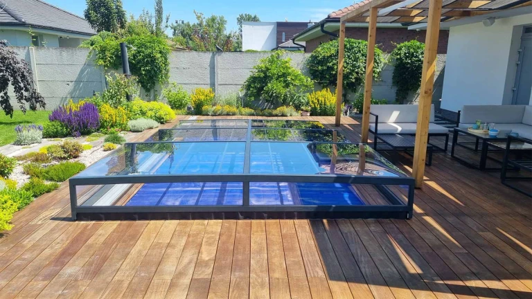 Une verrière moderne et basse surplombant la piscine, installée sur une terrasse en bois dans le jardin