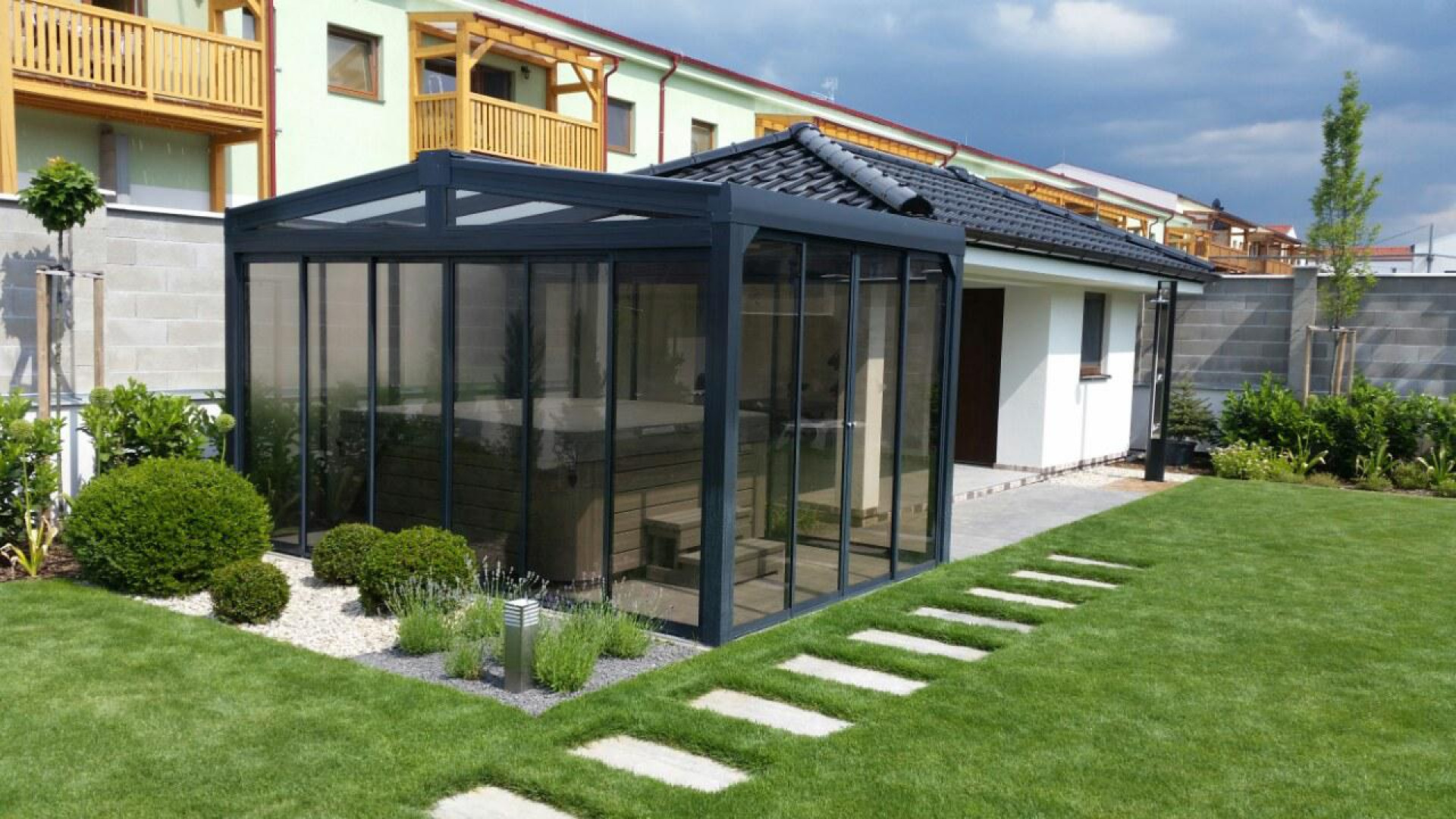Un abri moderne et vitré pour jacuzzi, doté d'une structure sombre, dans le jardin aménagé près de la maison.