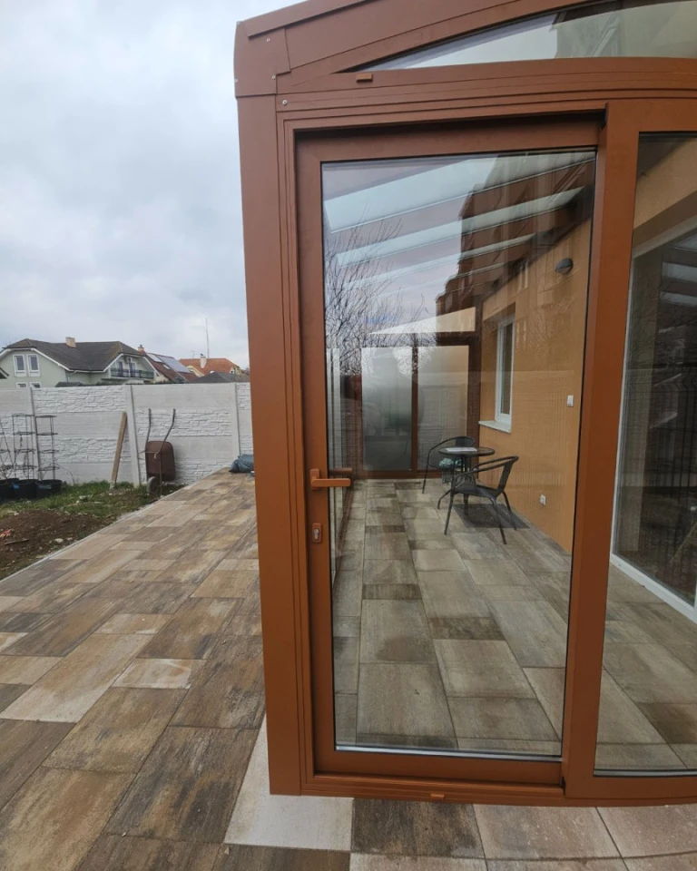 Vue détaillée de la structure en aluminium marron et des portes vitrées d'une véranda moderne située sur la terrasse.