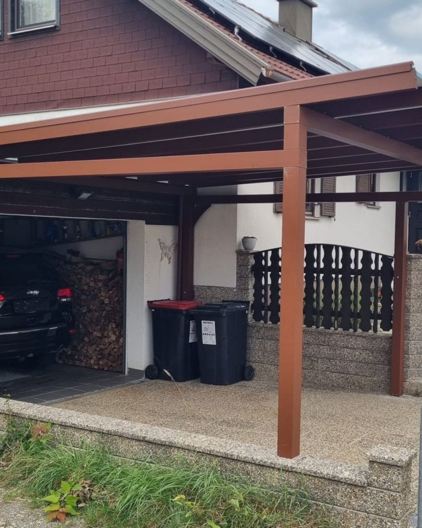 Un abri à voiture marron à côté d'une maison individuelle avec garage et poubelles