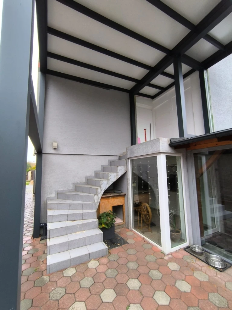 Structure moderne en aluminium formant un auvent au-dessus de l'escalier extérieur et de la terrasse d'une maison individuelle