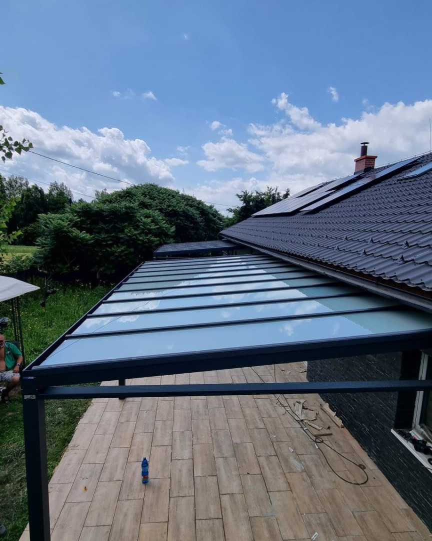 Une pergola moderne en aluminium avec un toit en verre, attenante à une maison individuelle et offrant une vue sur le jardin.