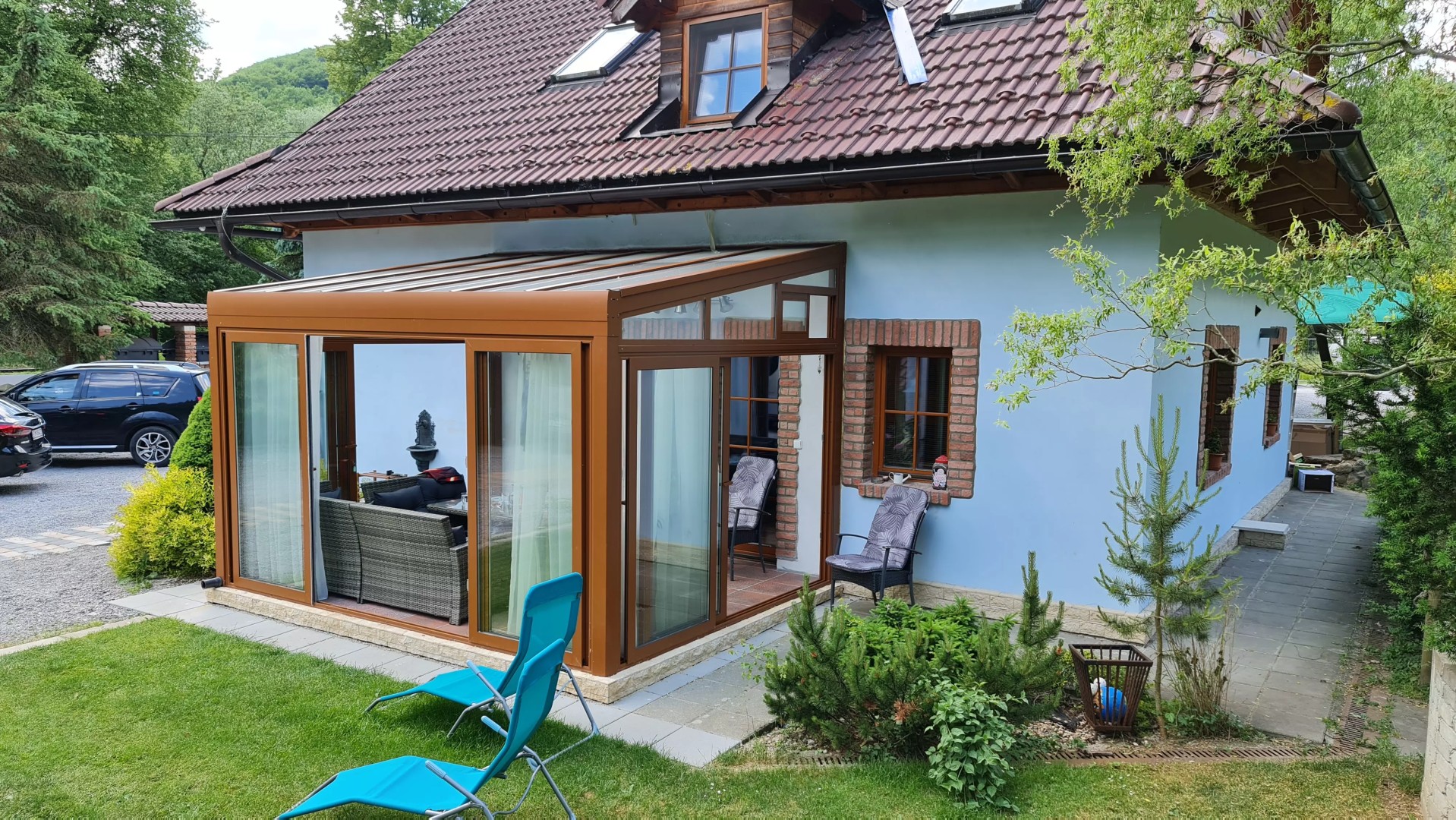 Une pergola en aluminium vitrée ROBUST de couleur marron, adossée à une maison individuelle et équipée de mobilier de jardin.