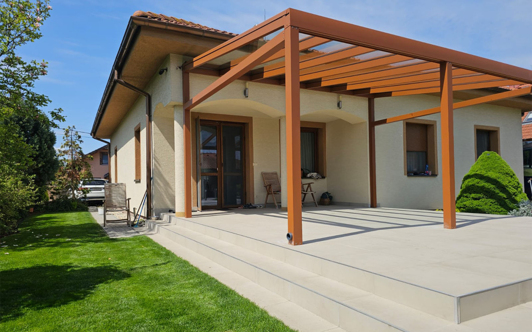 Une pergola moderne en aluminium de couleur marron, dotée d'un toit vitré, attenante à une maison individuelle et dotée d'une terrasse spacieuse.