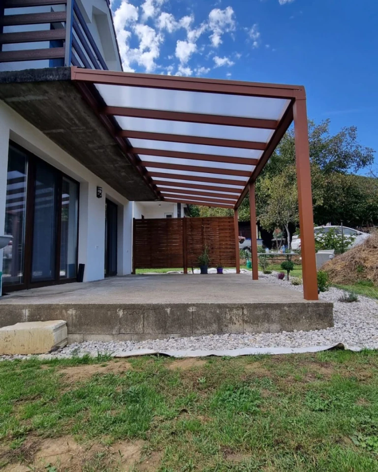 Une pergola moderne en aluminium marron, dotée d'une toiture claire, installée sur la terrasse en béton d'une maison individuelle.