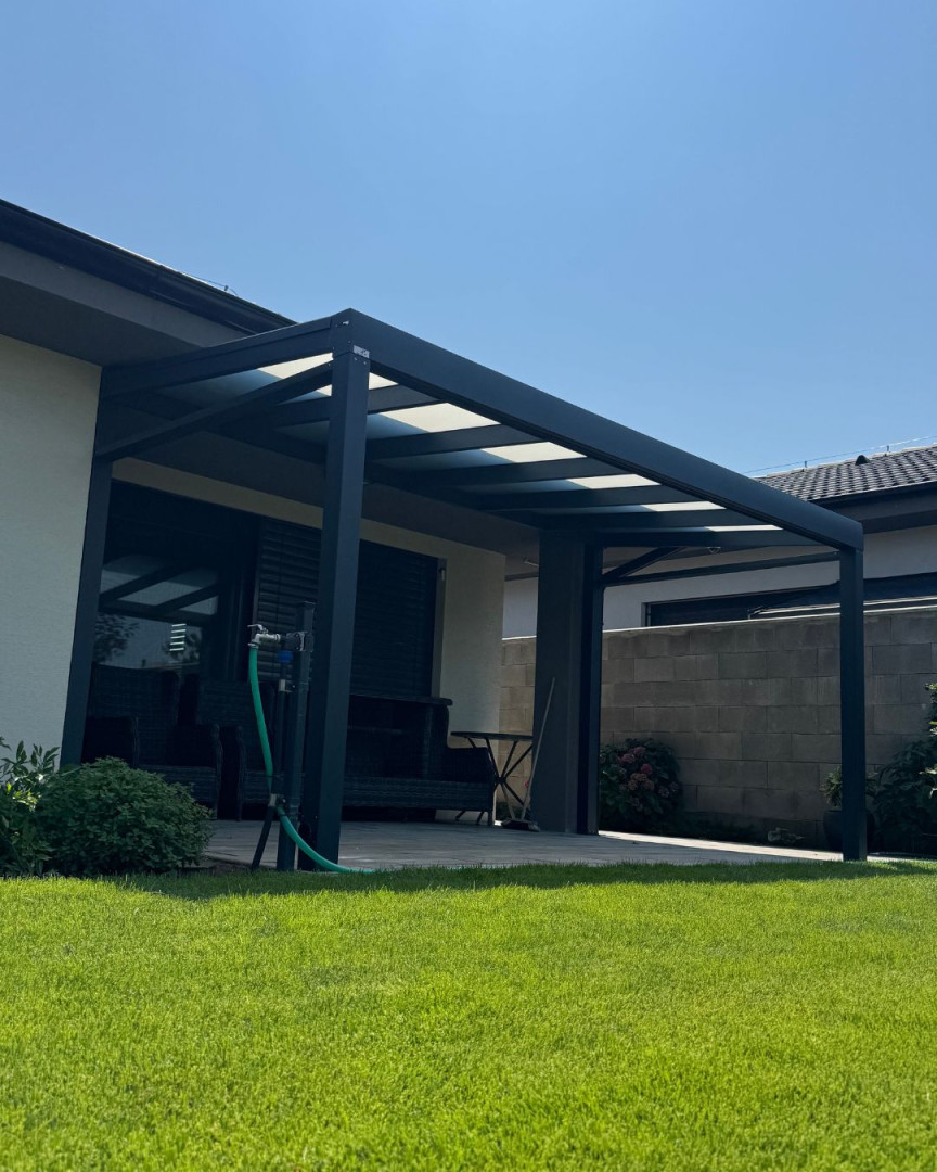 Une pergola moderne en aluminium gris foncé, attenante à la maison, avec un toit en verre et une pelouse bien entretenue