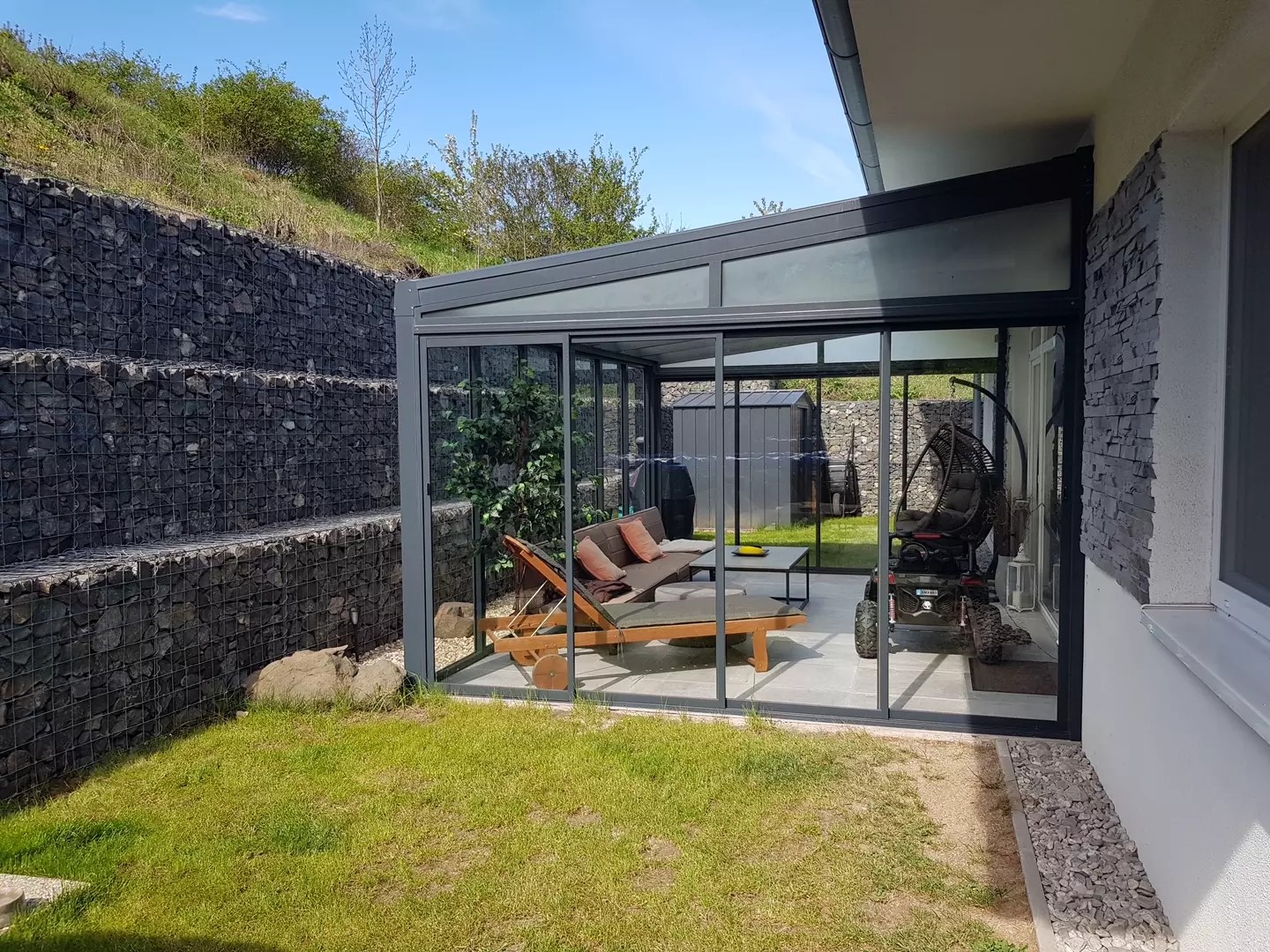 Une pergola moderne en aluminium avec une toiture en verre et un système coulissant, située à côté d'une maison à Braňany.
