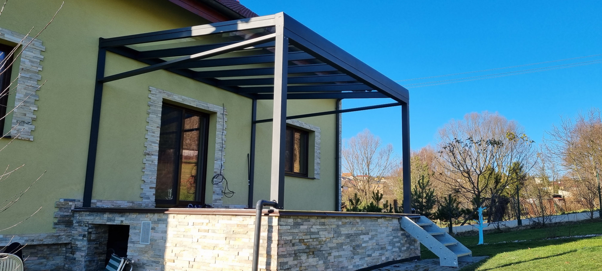 Pergola ROBUST moderne en aluminium gris foncé avec toit en verre, installée sur la terrasse d'une maison individuelle.