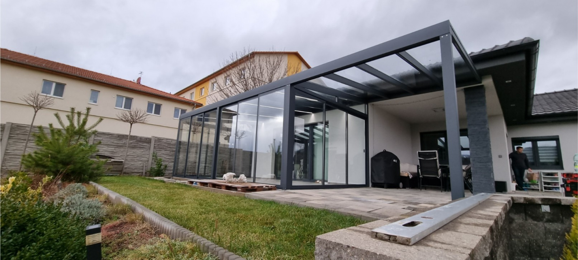 Une pergola moderne en aluminium et verre, avec une structure anthracite, construite près d'une maison individuelle à Klášterec.