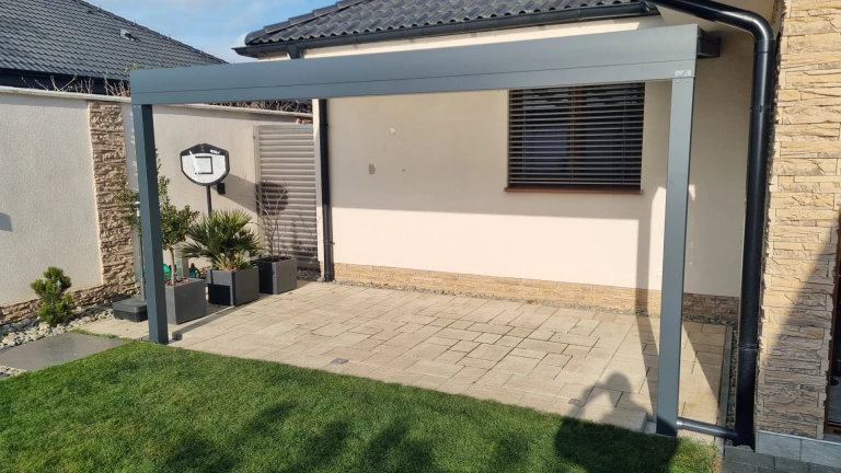Une pergola moderne en aluminium gris au-dessus de la terrasse d'une maison individuelle, avec un dallage et une pelouse