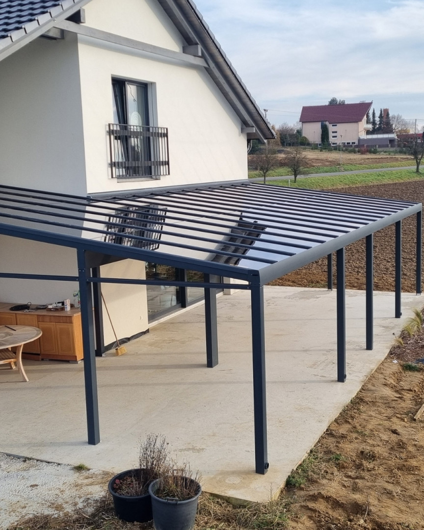 Une pergola moderne en aluminium gris foncé avec un toit en verre, installée près d'une maison individuelle à Senec.