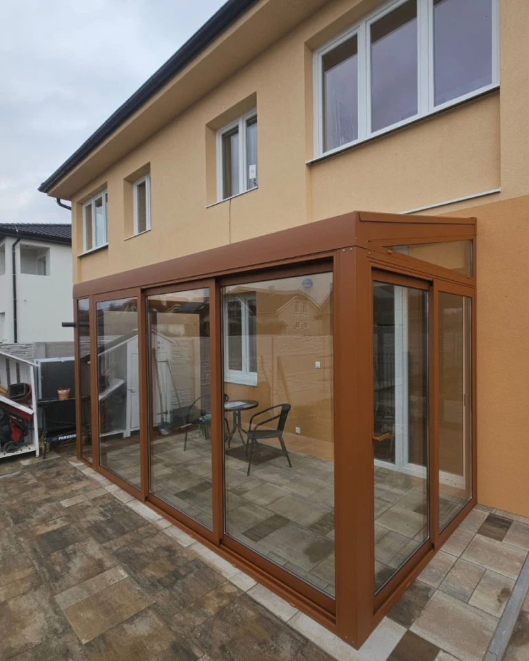 Une extension moderne vitrée attenante à une maison individuelle, avec une structure marron et des portes coulissantes.
