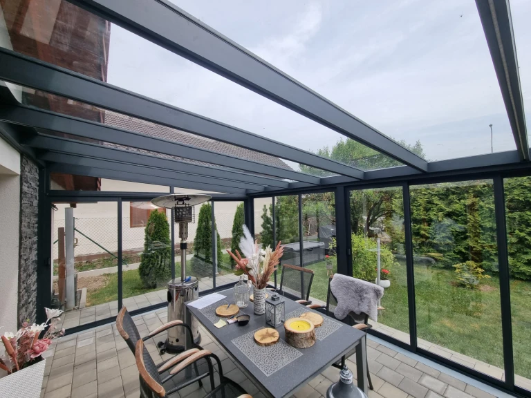 Une véranda moderne vitrée, dotée d'une structure en aluminium anthracite, d'une table à manger et d'une vue sur la verdure