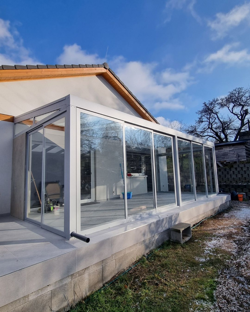 Une véranda moderne vitrée, dotée d'une structure en aluminium, attenante à une maison individuelle